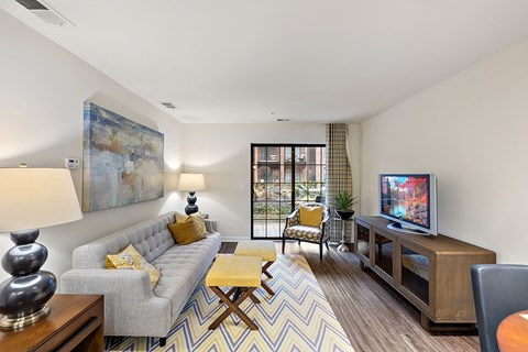 A living room with a grey couch, a yellow cushion, a wooden coffee table, a television, and a painting on the wall.